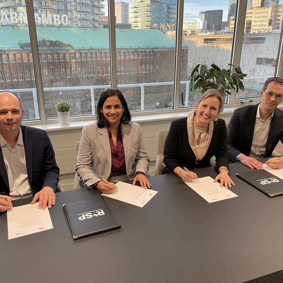 Four people are sitting at a table in a modern meeting room signing official documents. On the table are folders and papers bearing the “RSP” logo. In the background is a large window overlooking urban buildings, including one with the inscription “ABN AM